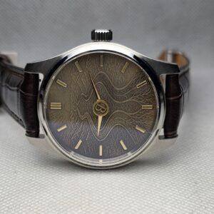 Custom milestone watch with a root-like textured dial and restrained central monogram