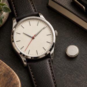 Editorial illustration of an unbranded analogue watch with an ivory dial and red seconds hand beside a silver button battery