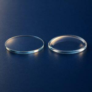 Editorial illustration of two transparent round watch crystals with different profiles on a dark blue surface