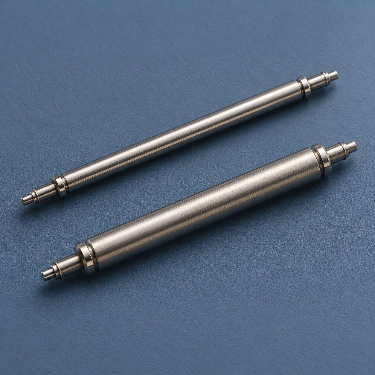 Editorial illustration of two silver-coloured watch spring bars with different tube thicknesses on a blue surface