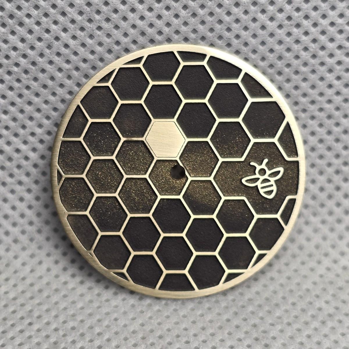 Honeycomb dial with raised brass outlines, a small bee and a textured dark background